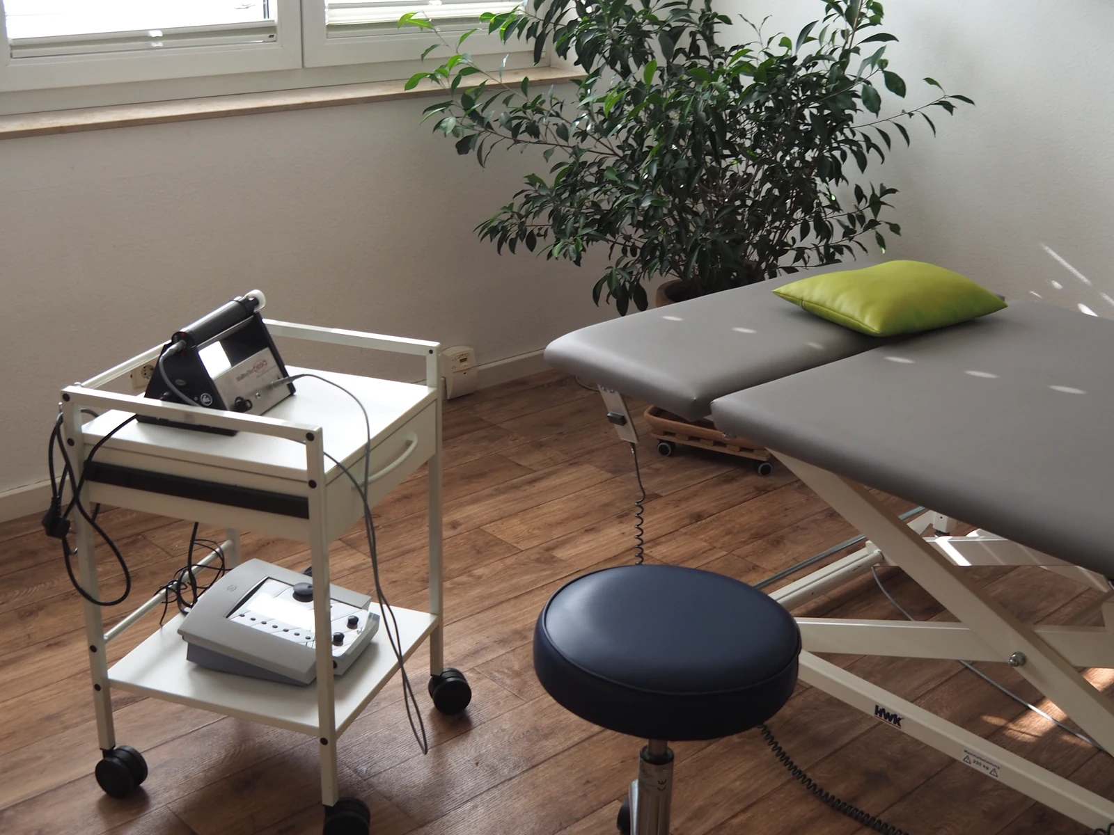 Elektrotherapiegerät auf einem Wagen neben der Behandlungsliege